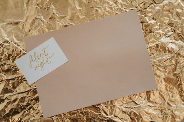 Stylish flatlay of a 'Silent Night' card on textured gold foil background, perfect for holiday themes.