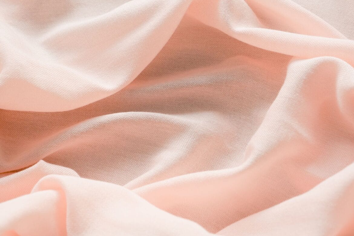 Close-up of pastel pink fabric with flowing folds, conveying softness and elegance.