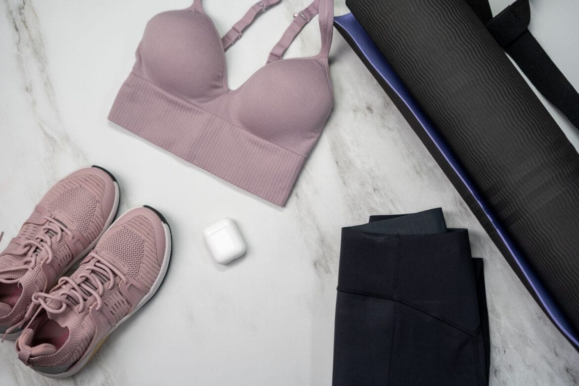 Pastel sports bra and sneakers with yoga mat and earphones on marble surface.