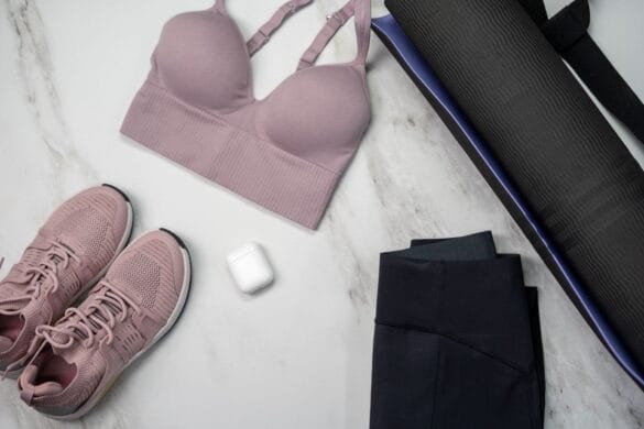 Pastel sports bra and sneakers with yoga mat and earphones on marble surface.